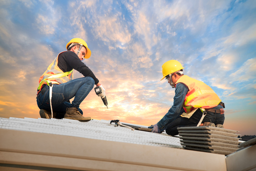Roofers working on a roof with safety equipment and tools